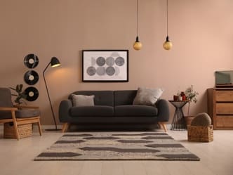 Modern living room interior design featuring dark gray sofa, warm beige walls, geometric circular wall art, brass pendant lights, and carefully arranged furniture with neutral color palette